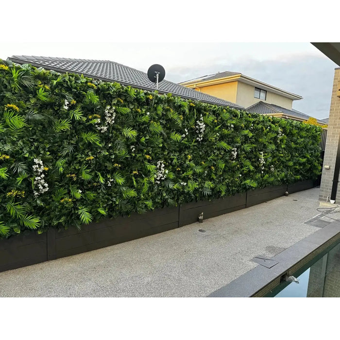 Artificial plant wall with diverse green foliage and white flowers by a modern poolside