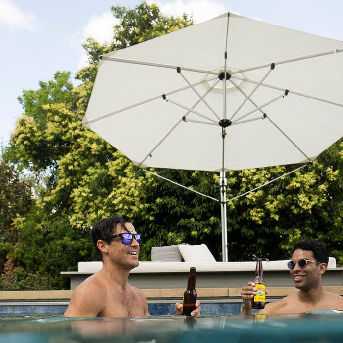 Two men relaxing with beers in a swimming pool under the shade of a white octagonal cantilever outdoor umbrella
