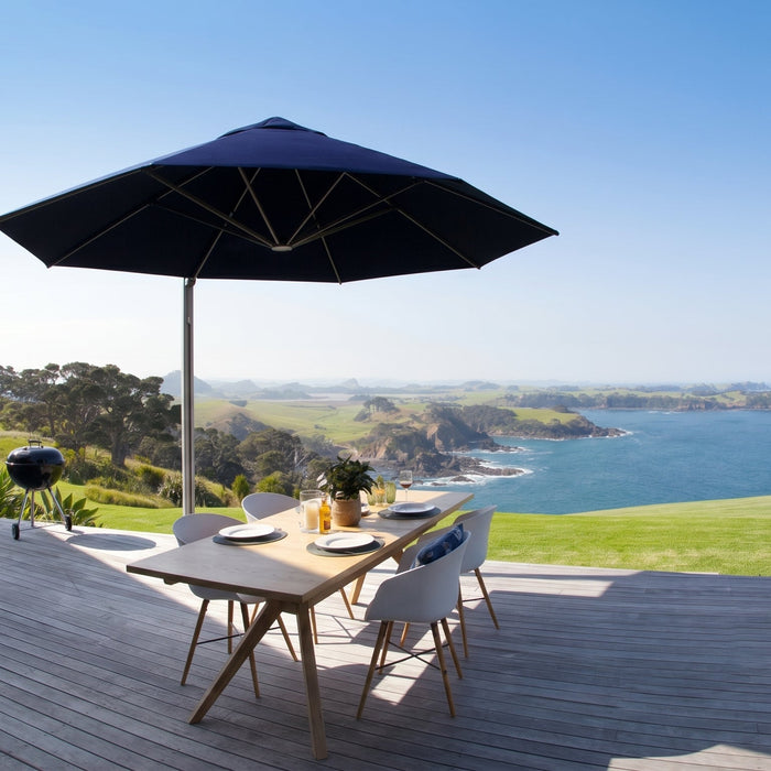 The Shadowspec Serenity with a Captain Navy canopy color providing shade over an outdoor dining area with a scenic view in the background