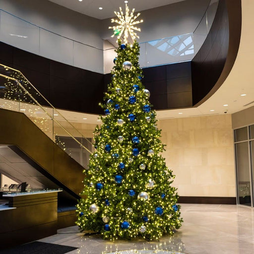 Decorated Commercial Christmas tree with blue and silver ornaments in a modern building interior.