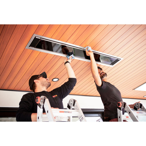 Two workers installing a ceiling recessed Bromic Platinum electric heater on a wooden ceiling.