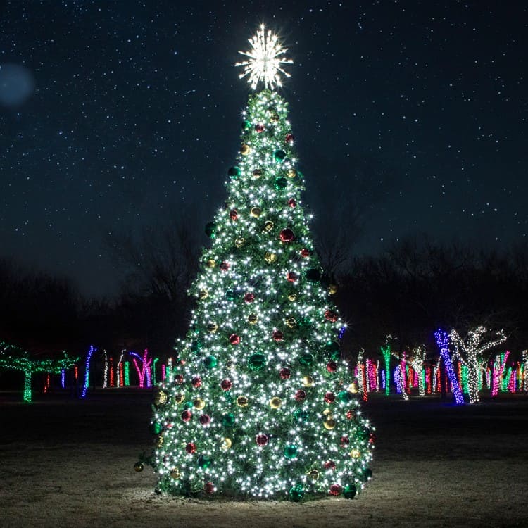 32 foot Decorated Christmas tree with lights and ornaments against a dark sky with star-like lights.