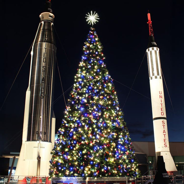 40 ft Decorated Commercial Christmas tree with two rocket models on either side at night.