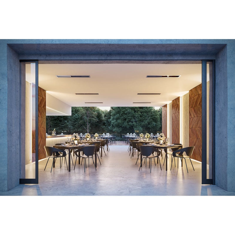 Modern indoor dining area with large glass doors and 6 Bromic Heaters recessed into the ceiling, leading to an outdoor garden.