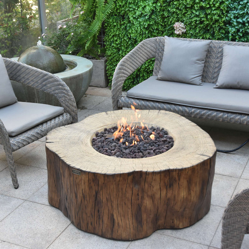 Outdoor patio setting with wicker chairs, a fire pit, and greenery.