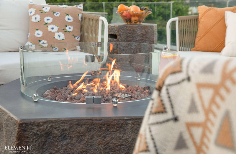 Outdoor patio with Elementi Columbia fire pit table, cushions, and fruit bowl on a clear day.