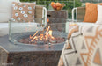 Outdoor patio with Elementi Columbia fire pit table, cushions, and fruit bowl on a clear day.