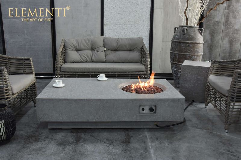 Outdoor patio setting with an Elementi fire pit table, chairs, and decorative elements.