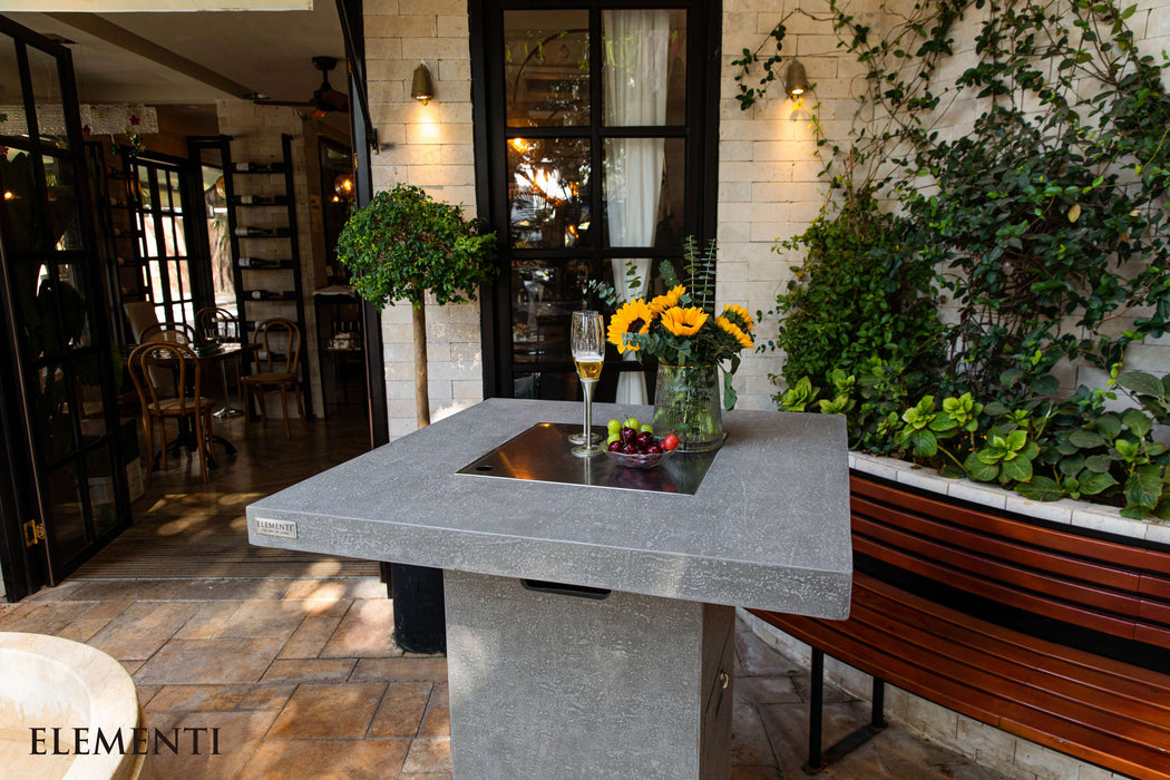 Outdoor setting with a Elementi Montreal stone table, flowers, and a glass of wine, surrounded by greenery.