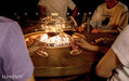 People around an Elementi Lafite fire pit table with glasses of wine, enjoying a warm evening together.