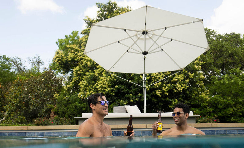 Two men relaxing with beers in a swimming pool under the shade of a white octagonal cantilever outdoor umbrella