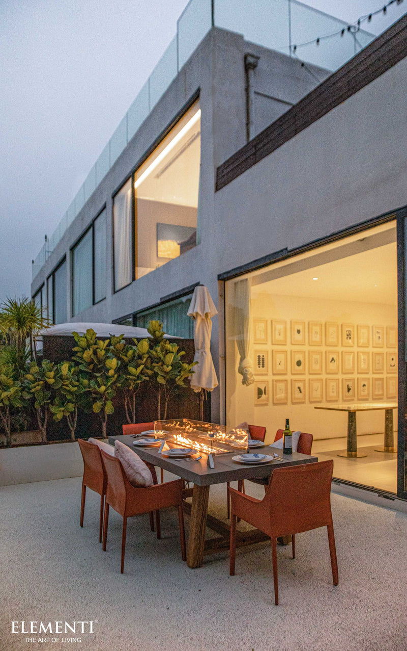Modern outdoor dining area with fire pit table in front of a house.