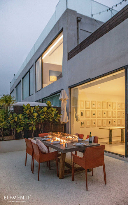 Modern outdoor dining area with fire pit table in front of a house.