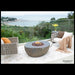 Outdoor patio with Elementi Boulder fire pit, chairs, and a view of water and trees