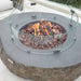 Round Elementi Boulder stone fire pit with glass cover on a patio, featuring the Elementi brand.