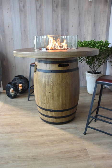 Elementi Lafite Wooden barrel table with fire pit on a wooden floor, surrounded by plants and lanterns.