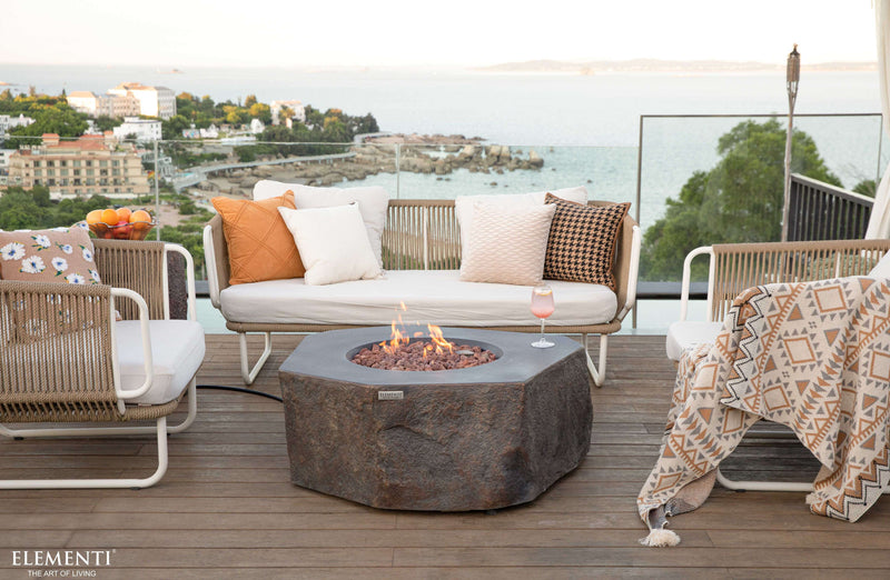 Outdoor patio setting with Elementi Columbia fire pit, chairs, and a scenic view.