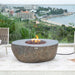 Fire pit table with flames on a patio overlooking a scenic view with chairs and a blanket.