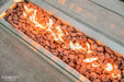 Fire pit with glowing red stones and flames on a concrete surface, featuring the Elementi brand.