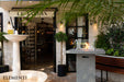 Outdoor setting with a fountain, bench, Elementi Montreal fire table, and building entrance.
