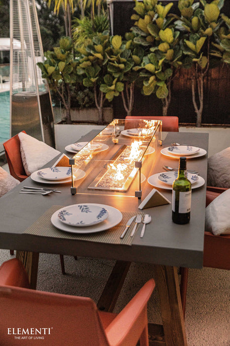 Elementi Sonoma Dining table set with plates, cutlery, and a bottle of wine on a fire pit table outdoors.