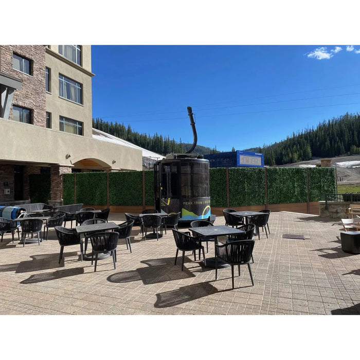 Outdoor seating area with black chairs and artificial green plant wall panels.