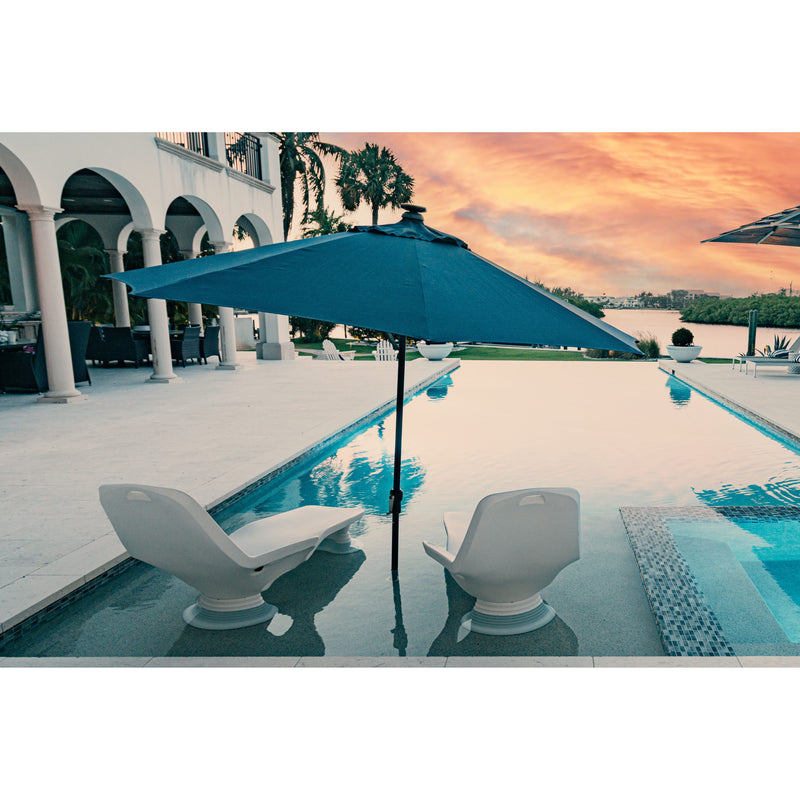Blue umbrella over two white TenJam sunloungers with risers by a pool with a sunset sky.