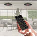 A person holding a smartphone displaying the Bromic Heating App interface, using it to adjust the settings of two circular, ceiling-mounted Eclipse Electric heaters in a modern outdoor patio setting