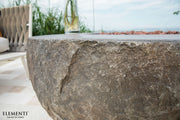 Close-up of a stone fire pit with 'Elementi' branding in an outdoor setting.