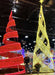 Person standing between a red spiral and yellow geometric Christmas tree decoration indoors.
