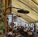 People dining outdoors under a large canopy with street view in the background and the focus placed on the Bromic Eclipse Heaters that are wall mounted