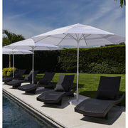 Black lounge chairs under white umbrellas by a pool with a hedge and sky background