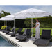 Woman adjusting a large white Helux market umbrella near lounge chairs by a pool