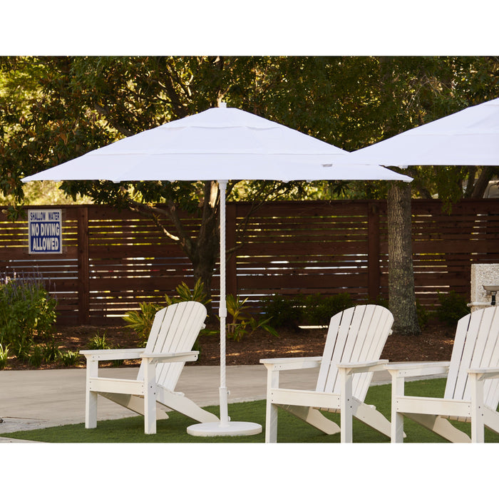 White Helux market patio umbrella and chairs on a patio with trees in the background