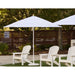 White Helux market patio umbrella and chairs on a patio with trees in the background