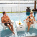Two people sitting on inflatable chairs in a pool with a scenic background