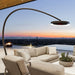 Outdoor patio with beige sofa, armchair, and a Bromic Eclipse Portable heater floor lamp overlooking a cityscape at sunset.