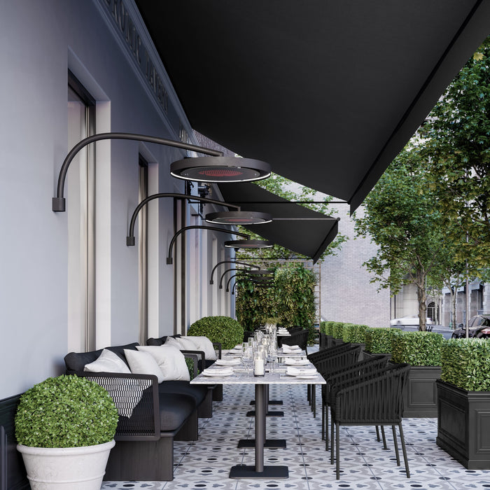 Outdoor dining area with black chairs, tables, and a black awning on a building with Bromic Eclipse Heaters mounted to the walls above the tables