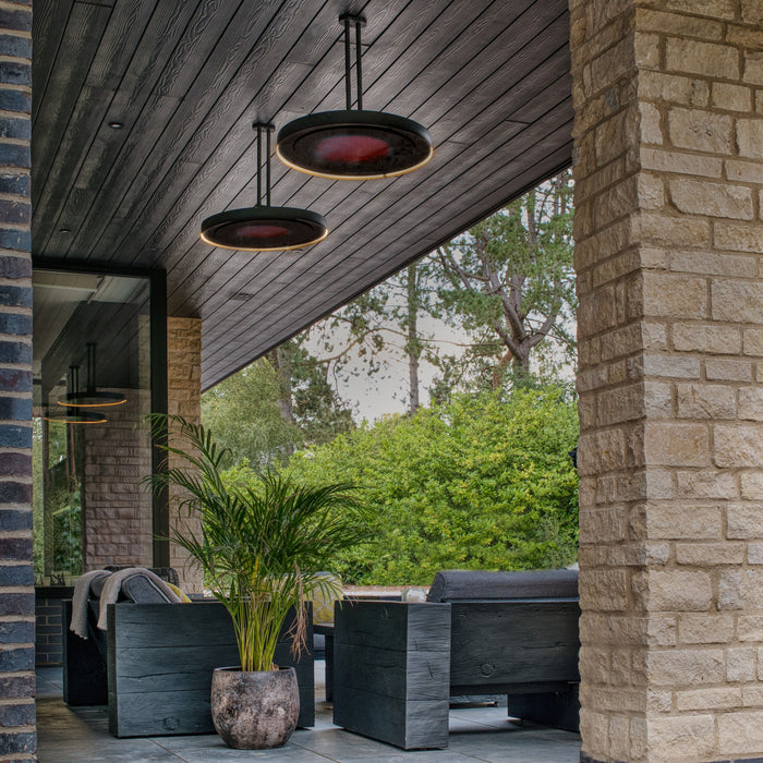 Outdoor patio area with modern furniture and pendant patio heaters that are also used as lights, featuring a stone wall and greenery.