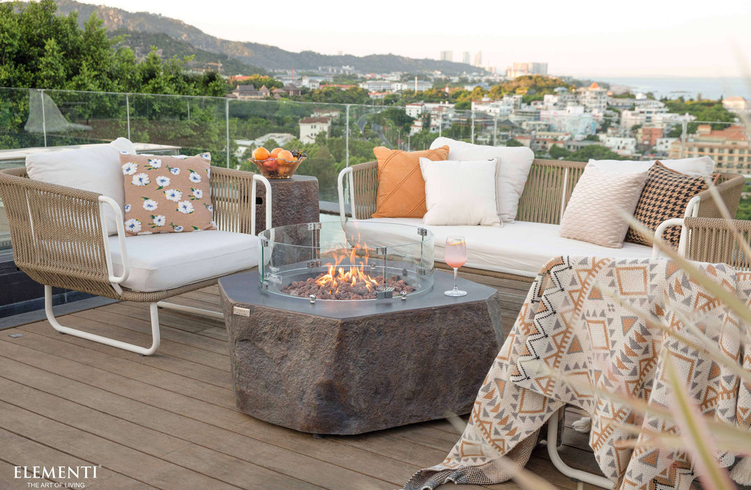 Outdoor patio setup with Elementi Columbia fire pit, chairs, and cushions on a wooden deck with cityscape view.