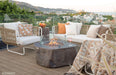 Outdoor patio setup with Elementi Columbia fire pit, chairs, and cushions on a wooden deck with cityscape view.