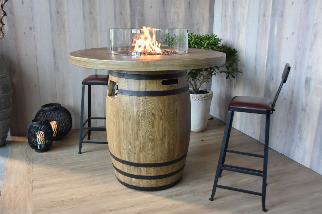 Wooden barrel Elementi Lafite table with fire pit in a room with stools and plants.