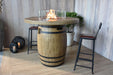 Wooden barrel Elementi Lafite table with fire pit in a room with stools and plants.