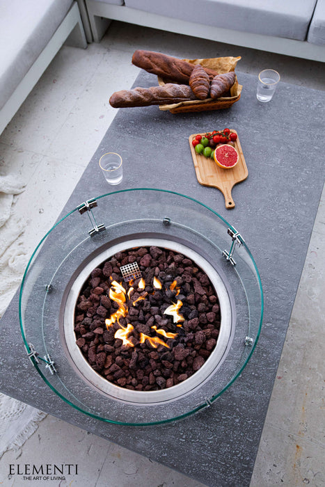 Outdoor fire pit table with flames, bread, and fruit on a concrete surface.