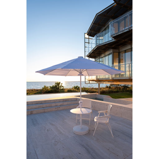 Outdoor patio set with a large Helux umbrella on a deck by a building and water.