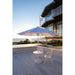 Outdoor patio set with a large Helux umbrella on a deck by a building and water.