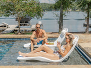 Man and woman lounging on TenJam Laylo Loungers by a pool with a lake view.