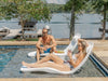 Man and woman lounging on TenJam Laylo Loungers by a pool with a lake view.