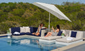 Two women relaxing on a patio with a pool, outdoor furniture, and a tilted ledge lounger umbrella.
