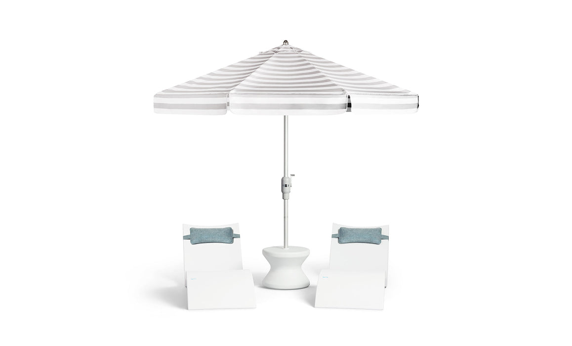 Ledge Lounger outdoor furniture set. Includes: Striped patio umbrella with two matching white Ledge Signature Chaises with headrest pillows on a white background